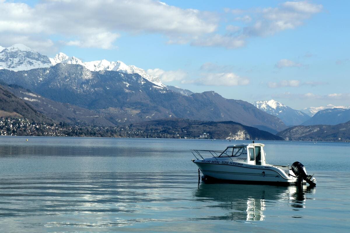 Bateau à moteur sur le lac d’Annecy en hiver avec vue sur les montagnes enneigées